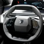 Bestuurders zicht op de cockpit van de 2025 Peugeot 5008 met compact stuurwiel met Peugeot logo en gebogen digitaal display dat 18.0 graden toont