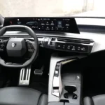 Breed interieurzicht van het dashboard van de 2025 Peugeot 5008 met volledig gebogen displayscherm, compact stuurwiel en moderne middenconsole indeling