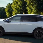 Volledig zijprofiel van witte 2025 Peugeot 5008 familie SUV met verlengde lengte, zwart dak en moderne SUV proporties op stadsstraat