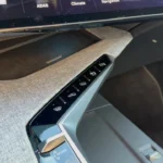 Schuine weergave van de middenconsole van de 2025 Peugeot 5008 met een rij verlichte piano toets-stijl aanraakbediening voor verschillende voertuigfuncties