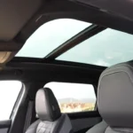 Brede hoek interieurzicht van de 2025 Peugeot 5008 met nadruk op grote panoramadak opening boven gestoffeerde voorstoelen