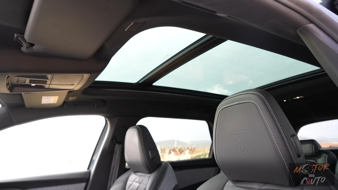 Brede hoek interieurzicht van de 2025 Peugeot 5008 met nadruk op grote panoramadak opening boven gestoffeerde voorstoelen