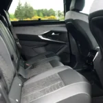 Interieurzicht van de tweede rij stoelen van de 2025 Peugeot 5008 met gestikt bekledingspatroon en individuele armleuningen met raamzicht