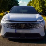Vooraanzicht van witte 2025 Peugeot 5008 met kenmerkend LED koplamp ontwerp, Peugeot grille en moderne voorbumper op landelijke weg