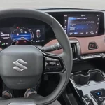 Bestuurdersview van de 2025 Suzuki e Vitara met leren stuurwiel met bedieningselementen en 10,25-inch digitaal instrumentarium
