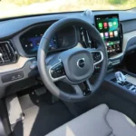 2026 Volvo XC60 bestuurders gezichtspunt met Apple CarPlay op touchscreen, digitaal dashboard en stuurwiel vanuit bestuurdersstoel perspectief