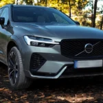 2026 Volvo XC60 dynamische voor driekwart hoek met vernieuwd grille ontwerp, zelfverzekerde houding en Forest Lake metallic lak op bosweg