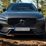 2026 Volvo XC60 vooraanzicht met nieuw diagonaal grille ontwerp, Thor's Hammer LED koplampen en grijze metallic lak in bosomgeving