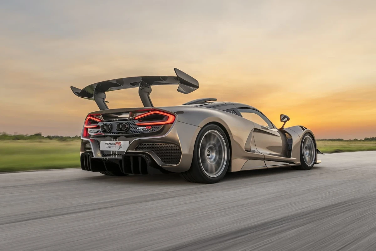 Dynamische achter driekwart zicht van Hennessey Venom F5 Revolution LF in champagne metallic lak met grote achterspoiler, agressieve aerodynamica, en bewegingsonscherpte op circuit