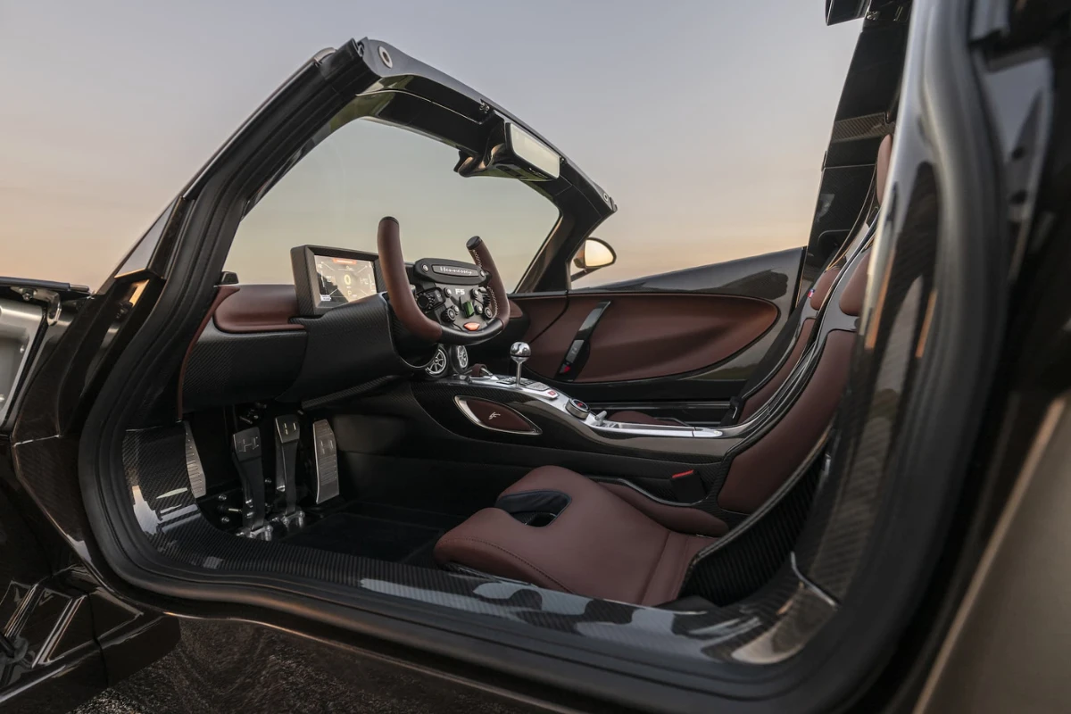 Interieurzicht van Hennessey Venom F5 Revolution LF met bruine leren stoelen, koolstofvezel dashboard, handgeschakelde versnellingspook, en bestuurder-gerichte cockpit ontwerp met vleugeldeuren open