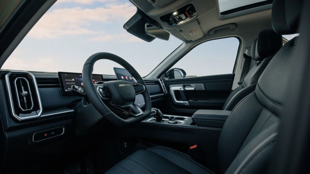 Jaecoo 7 SUV interieur vanaf bestuurderszijde met zwarte leren stoelen, digitaal dashboard display, stuurwiel met Jaecoo-branding, centraal touchscreen en panoramadak met bewolkte lucht zichtbaar