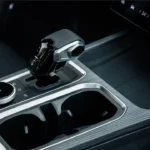 Jaecoo 7 SUV middenconsole met moderne versnellingspook, roterende bedieningsknop, dubbele bekerhouders, koolstofvezel-stijl trim, leren stoelen en dashboard touchscreen zichtbaar op achtergrond