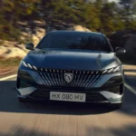 Dynamisch vooraanzicht van de 2025 Peugeot 308 facelift in grijs met verfijnde drieklauw LED-design en moderne front styling tijdens het rijden