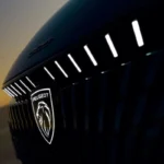 Close-up detail van het verlichte Peugeot leeuw embleem op de nieuwe 308 facelift met LED lichtstrips erboven die een premium verlichtingssignatuur creëren