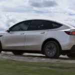 Witte Tesla Model YL vanuit achter driekwart hoek met verlengde afmetingen, herontworpen achterspoiler en grotere achterklep van de 6-zits elektrische SUV