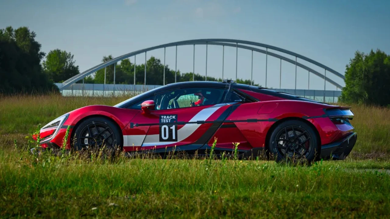 Rode Yangwang U9 Track Edition elektrische supercar met Track Test 01 livery gepositioneerd op gras met moderne brugarchitectuur op de achtergrond bij Duitse testfaciliteit