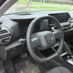 Bestuurderscockpit zicht van 2025 Citroën C4 met digitaal instrumentenpaneel, lederen stuurwiel met vernieuwd logo en fysieke klimaatregelaars