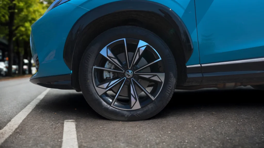 Detailopname van 2025 MG HS 19-inch lichtmetalen velg met diamant-geslepen spakendesign, MG merk naafkap en band zijwand op Arctic Blue voertuig