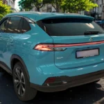 Achteraanzicht van 2025 MG HS Hybrid+ in Arctic Blue op stadsstraat, met doorlopende LED-achterlichtbalk, MG-logo, Hybrid+ badge en Europese kentekenplaat houder