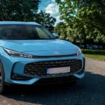 Zijaanzicht van 2025 MG HS Hybrid+ SUV in Arctic Blue geparkeerd in woonwijk, met coupé-achtige daklijn, chromen details en 19-inch diamant-geslepen lichtmetalen velgen