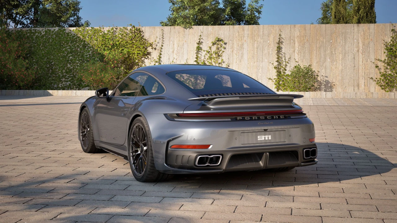 Zilveren 2025 Porsche 911 Turbo S vanuit achterste driekwart hoek in buitenomgeving met betonnen muur achtergrond, achterbumper en brede carrosserie ontwerp