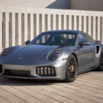 Zilveren 2025 Porsche 911 Turbo S Coupe in buitenomgeving met moderne gebouw achtergrond, voorste driekwart hoek met agressieve aerodynamische styling