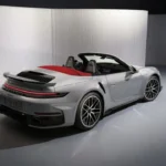 Zilveren 2025 Porsche 911 Turbo S Cabriolet vanuit achterste driekwart hoek met brede achterspatborden, actieve achterbumper, LED achterlichten en dubbele titanium uitlaat openingen in studio verlichting