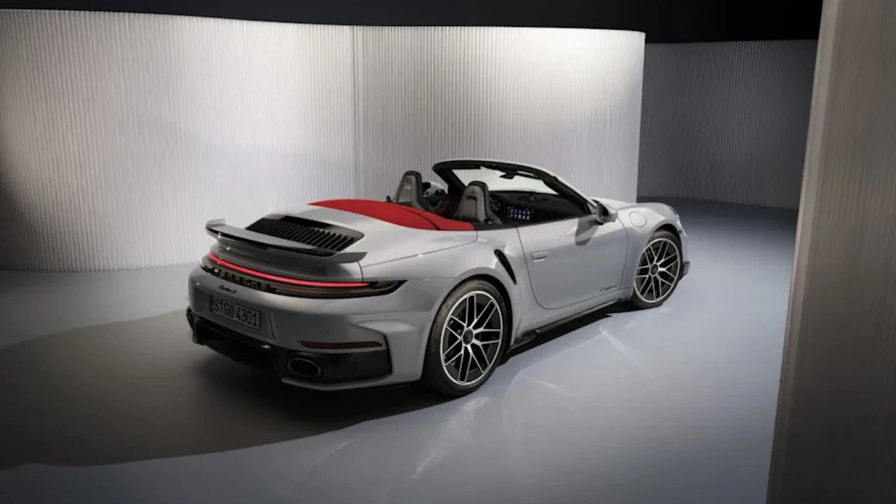 Zilveren 2025 Porsche 911 Turbo S Cabriolet vanuit achterste driekwart hoek met brede achterspatborden, actieve achterbumper, LED achterlichten en dubbele titanium uitlaat openingen in studio verlichting