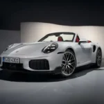 Zilveren 2025 Porsche 911 Turbo S Cabriolet cabrio sportwagen gefotografeerd vanuit voorste driekwart hoek in studio-omgeving, met agressief voorbumper ontwerp, LED koplampen en rood leren interieur