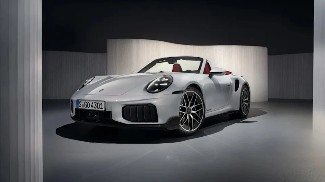 Zilveren 2025 Porsche 911 Turbo S Cabriolet cabrio sportwagen gefotografeerd vanuit voorste driekwart hoek in studio-omgeving, met agressief voorbumper ontwerp, LED koplampen en rood leren interieur
