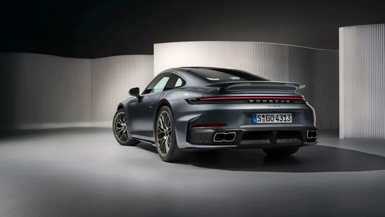 Metallic grijze 2025 Porsche 911 Turbo S Coupe vanuit achterste driekwart met actieve achterbumper, brede achterspatborden, LED achterlichtbalk en dubbele uitlaat openingen