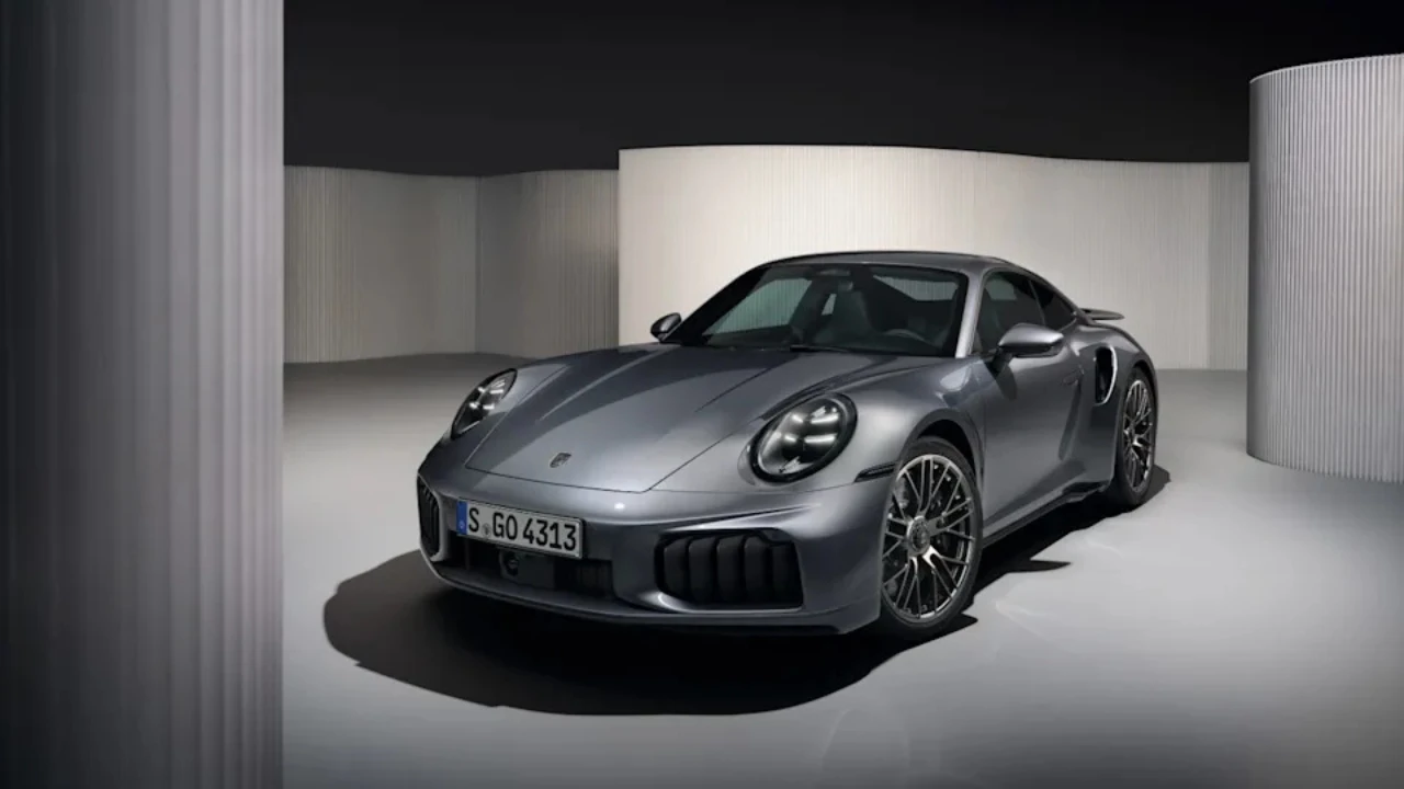 Metallic grijze 2025 Porsche 911 Turbo S Coupe vanuit voorste driekwart hoek in studio-omgeving, met brede voorbumper met grote luchtinlaten, LED koplampen en agressief aerodynamisch ontwerp