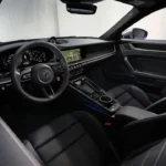 Interieur passagier aanzicht van 2025 Porsche 911 Turbo S met dashboard, middenconsole, sportstoelen, carbon fiber trim en modern infotainment systeem