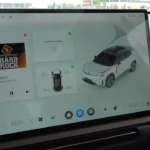 Hoofd infotainment scherm met media afspelen (Hardrock van Bauer Media), 3D voertuig visualisatie, klimaatregeling interface, en de uitgebreide integratie van entertainment en voertuig systemen.