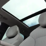 Interieur aanzicht met nadruk op het panoramisch schuifdak dat het ruimtelijke gevoel van de 2,85m wielbasis cabine versterkt, met Harman Kardon luidsprekers geïntegreerd in hoofdsteunen en premium bekleding door het geheel.