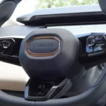 Gedetailleerd aanzicht van het stuurwiel met de Lynk & Co branding met bronzen accent, multifunctionele bedieningsknoppen voor cruise control, media, en bestuurders assistentie systemen, en de premium leren afwerking.