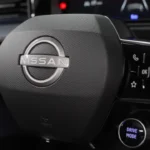 Close-up van Nissan Micra stuurwiel met Nissan-logo in het midden, bedieningsknoppen op spaken en Drive Mode-knop zichtbaar