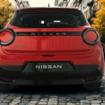 Volledig achteraanzicht van rode 2026 Nissan Micra op kasseienstraat met compleet achterontwerp met ronde achterlichten en Nissan-branding