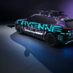 Achter driekwart weergave van gecamoufleerde 2026 Porsche Cayenne Electric met digitaal patroon livery gepositioneerd boven draadloze oplaadpad, wat het achterontwerp van het voertuig en draadloze oplaadmogelijkheden benadrukt
