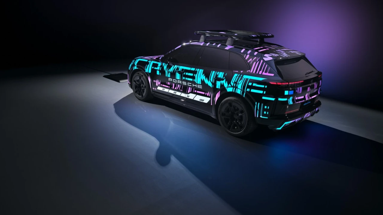 Achter driekwart weergave van gecamoufleerde 2026 Porsche Cayenne Electric met digitaal patroon livery gepositioneerd boven draadloze oplaadpad, wat het achterontwerp van het voertuig en draadloze oplaadmogelijkheden benadrukt