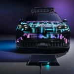 Vooraanzicht van de 2026 Porsche Cayenne Electric prototype gepositioneerd boven de draadloze oplaadpad, wat de precieze uitlijning benadrukt die nodig is voor optimaal functioneren van het 11kW inductieve oplaadsysteem.