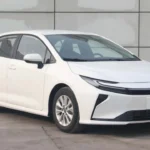 Witte 2026 Toyota Corolla sedan voorkant drie-kwart aanzicht met nieuwe gesplitste koplampen met C-vormige LED strips, herontworpen bumper met kleinere luchtinlaat, en moderne styling geïnspireerd door Prius design taal