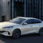 Witte BYD Seal 6 DM-i sedan gefotografeerd vanuit voorkant driekwart hoek met Ocean-serie ontwerpelementen, gesloten grille, LED-koplampen en zwarte aerodynamische wielen tegen moderne architectuur achtergrond