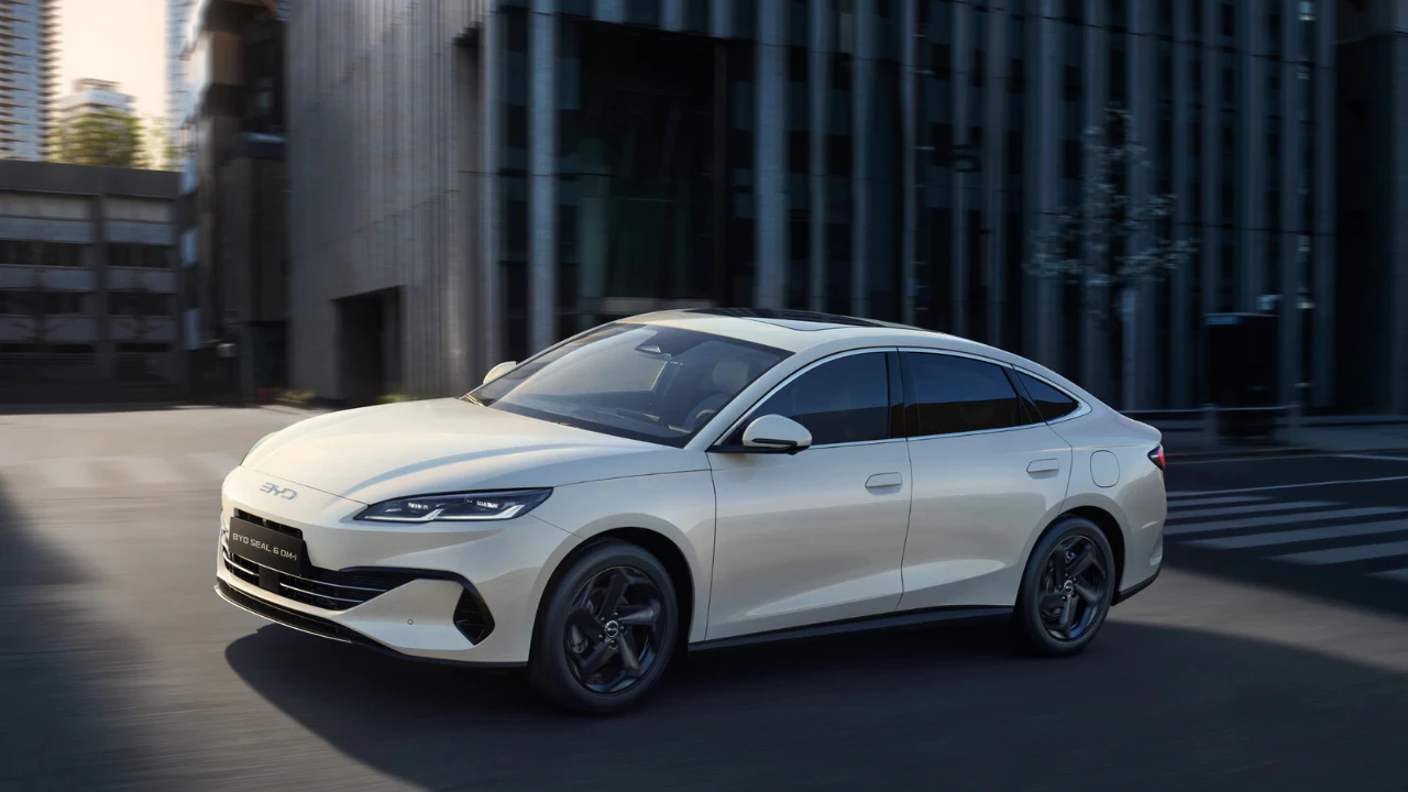 Witte BYD Seal 6 DM-i sedan gefotografeerd vanuit voorkant driekwart hoek met Ocean-serie ontwerpelementen, gesloten grille, LED-koplampen en zwarte aerodynamische wielen tegen moderne architectuur achtergrond