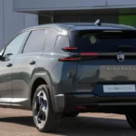 Grijze Citroën C5 Aircross SUV gepositioneerd bij elektrisch voertuig-laadstation met moderne architectuur achtergrond, benadrukt elektrificatiestrategie en duurzame transportoplossingen