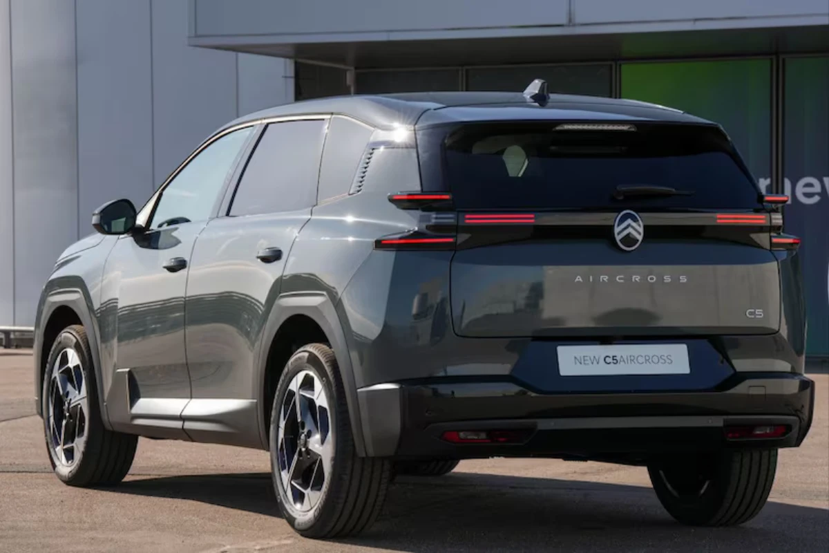 Grijze Citroën C5 Aircross SUV gepositioneerd bij elektrisch voertuig-laadstation met moderne architectuur achtergrond, benadrukt elektrificatiestrategie en duurzame transportoplossingen