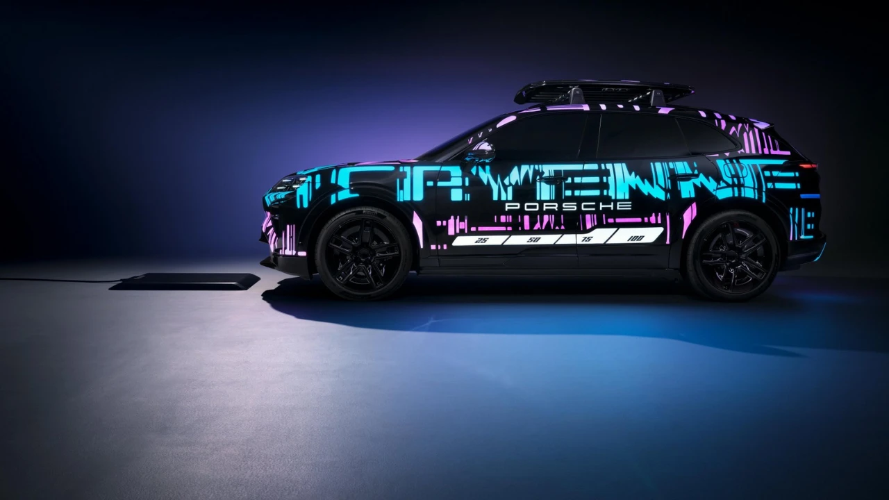 Zijaanzicht van 2026 Porsche Cayenne Electric prototype met cyaan en paarse digitale camouflage livery gepositioneerd boven draadloze oplaadpad, met PORSCHE branding en dakaccessoires