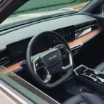 Interieurzicht van 2025 KGM Torres Hybrid met grijze lederen stoelen, dubbele 12,3-inch touchscreen displays, driespaaks stuurwiel met KGM-logo, zwevende middenconsole met oranje accent afwerking en horizontale ventilatieroosters