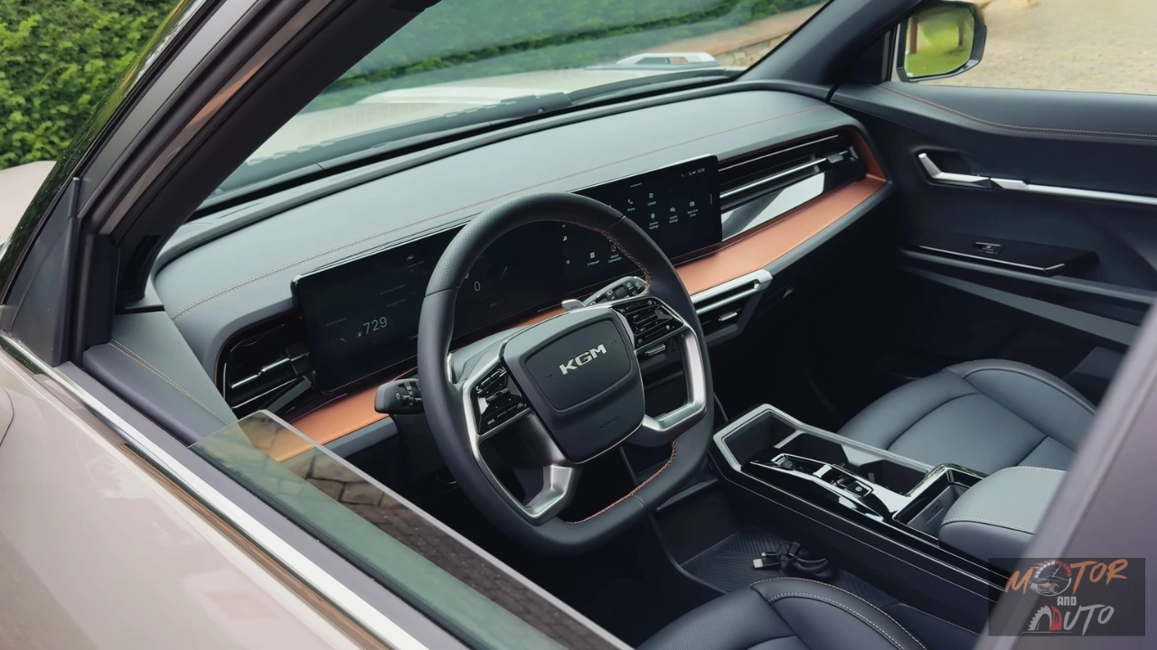 Interieurzicht van 2025 KGM Torres Hybrid met grijze lederen stoelen, dubbele 12,3-inch touchscreen displays, driespaaks stuurwiel met KGM-logo, zwevende middenconsole met oranje accent afwerking en horizontale ventilatieroosters