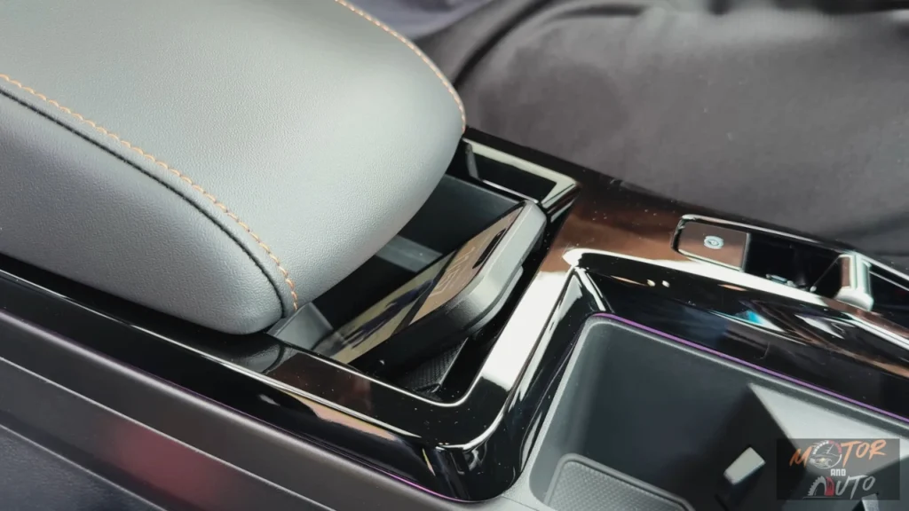 Bovenaanzicht van 2025 KGM Torres Hybrid middenconsole met draadloze oplaadplaat met rubber grip oppervlak, verchroomde bekerhouders en opbergvakken met oranje accentverlichting